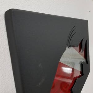 Puede incluir: Arte de pared de metal negro con un dise&ntilde;o recortado de un pez. El pez es rojo y blanco con un contorno negro. El arte est&aacute; montado en una pared blanca.