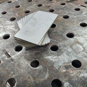 Pu&ograve; includere: Un mucchio di piastre di metallo argentate su una superficie di metallo con fori. La superficie &egrave; usurata e di colore grigio.