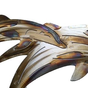 May include: Metal wall art sculpture of two dolphins leaping out of the water. The dolphins are made of brushed metal with a brown and gold finish.