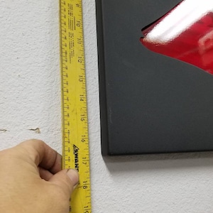 Puede incluir: Una cinta m&eacute;trica amarilla con marcas negras est&aacute; unida a una pared blanca. La cinta est&aacute; marcada en pulgadas y tiene aproximadamente 18 pulgadas de largo.