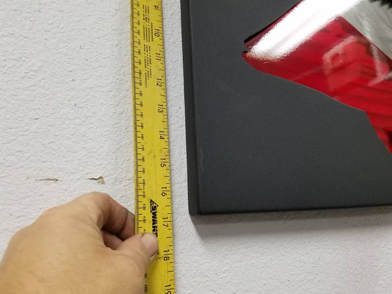 Puede incluir: Una cinta m&eacute;trica amarilla con marcas negras est&aacute; unida a una pared blanca. La cinta est&aacute; marcada en pulgadas y tiene aproximadamente 18 pulgadas de largo.