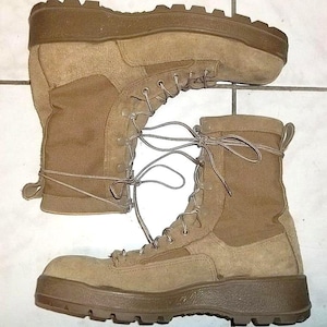 Könnte beinhalten: Ein Paar beigefarbene taktische Stiefel mit einem Obermaterial aus Wildleder und Canvas, einem hohen Schnürdesign mit Metallösen und einer dicken, dunkelbraunen Gummisohle mit tiefem Profil für verbesserte Bodenhaftung und Stabilität.
