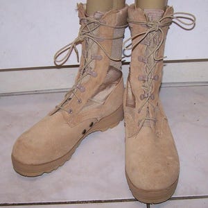 Puede incluir: Un par de botas tácticas de ante y lona color canela con diseño de caña alta, punteras redondas reforzadas y sistema de cordones con ojales metálicos. Las botas tienen una suela de goma gruesa y texturizada y paneles laterales de ventilación.