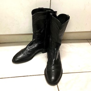 Op de afbeelding: Een paar zwarte leren cowboylaarzen met een textuur van hagedissenhuid op de voet en schacht. De laarzen hebben een puntige neus, een halverwege de kuit hoogte, treklussen aan de bovenkant en subtiele decoratieve stiksels langs de kraag.
