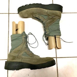 May include: A pair of sage green tactical boots featuring suede and fabric panels, black rubber soles, and matching green laces. Each boot contains a tan plastic shoe tree insert to maintain the shape of the high-top ankle collar.