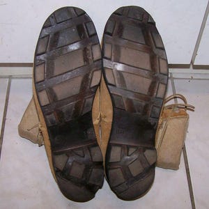 K&ouml;nnte beinhalten: Nahaufnahme der Sohlen eines Paares brauner Lederstiefel mit einem braunen Gummibrockenmuster. Die Stiefel haben ein braunes Leder-Obermaterial und einen beigefarbenen Canvas-Kn&ouml;chelriemen. Die Gr&ouml;&szlig;e "8R" ist auf der Sohle des rechten Stiefels aufgedruckt.