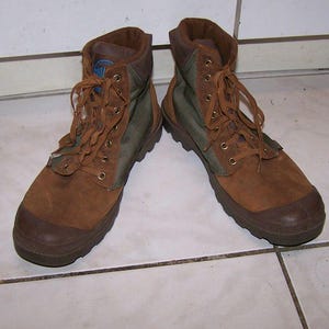 May include: A pair of brown and olive green boots with laces. The boots have a suede-like texture on the upper and a rubber sole. The boots are designed for outdoor activities and have a high-top design.