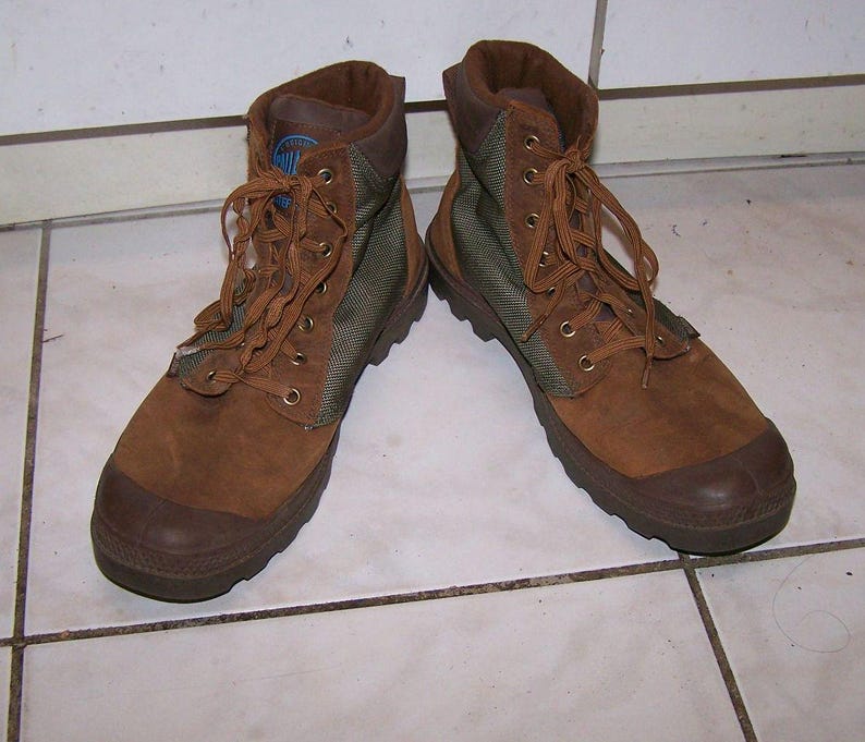 May include: A pair of brown and olive green boots with laces. The boots have a suede-like texture on the upper and a rubber sole. The boots are designed for outdoor activities and have a high-top design.