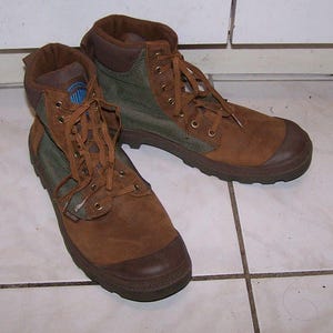 May include: A pair of brown suede boots with olive green canvas accents. The boots have brown laces, a rubber toe cap, and a padded collar. The boots are designed for outdoor activities.