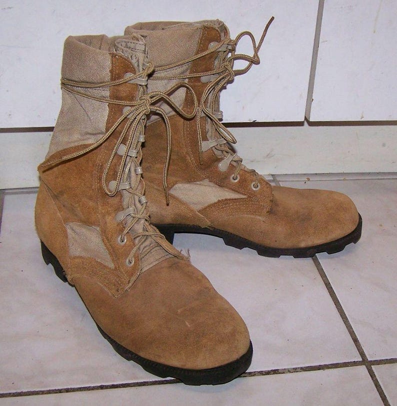 K&ouml;nnte beinhalten: Ein Paar braune Lederstiefel mit braunen Canvas-Akzenten und Schn&uuml;rsenkeln. Die Stiefel haben ein robustes, abgenutztes Aussehen.