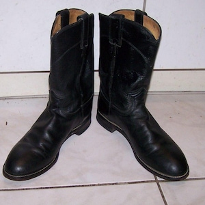 May include: A pair of black leather cowboy boots. The boots feature a classic design with pointed toes, stacked heels, and pull straps. The leather appears worn, suggesting regular use. The boots are set against a neutral background.