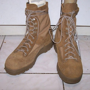 Puede incluir: Un par de botas de combate color canela con una construcción superior de ante y textil en un diseño de caña alta. Las botas incluyen un sistema de cierre con cordones, ojales metálicos y cordones estampados en marrón y canela, con suela de goma.