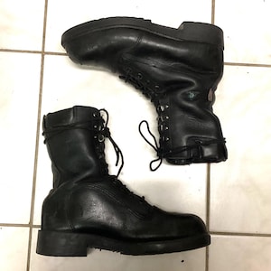 May include: A pair of black leather lace-up boots featuring a high-top design, rounded toes, thick rubber soles, and black laces. The boots have a textured finish on the side panels and a smooth leather construction throughout the upper portion.