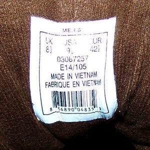 May include: A close-up of a white label with text and a barcode. The label includes size information: UK 8 1/2, USA 9 1/2, EUR 42 1/2. The label also states "MADE IN VIETNAM" and "FABRIQUE EN VIETNAM".