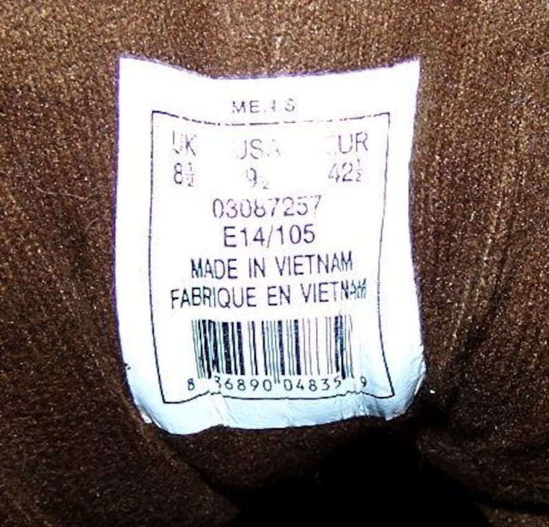 May include: A close-up of a white label with text and a barcode. The label includes size information: UK 8 1/2, USA 9 1/2, EUR 42 1/2. The label also states "MADE IN VIETNAM" and "FABRIQUE EN VIETNAM".