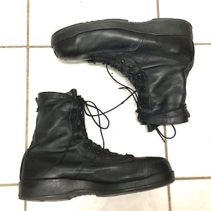 Puede incluir: Un par de botas tácticas de cuero negro con diseño de caña alta, punteras redondeadas reforzadas y suelas gruesas de goma negra. Las botas incluyen cordones negros que pasan por ojales metálicos hasta el tobillo para un ajuste seguro.