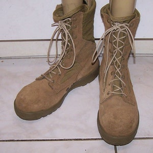 Puede incluir: Un par de botas tácticas de combate en ante y lona de color tostado, con caña alta, puntera redonda reforzada y cordones a juego pasados por ojales metálicos. Las botas tienen suelas gruesas de goma de color marrón oscuro.