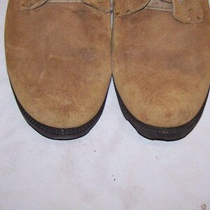 K&ouml;nnte beinhalten: Ein Paar braune Wildlederschuhe mit schwarzen Sohlen. Die Schuhe haben einen Schn&uuml;rverschluss und eine abgerundete Spitze.