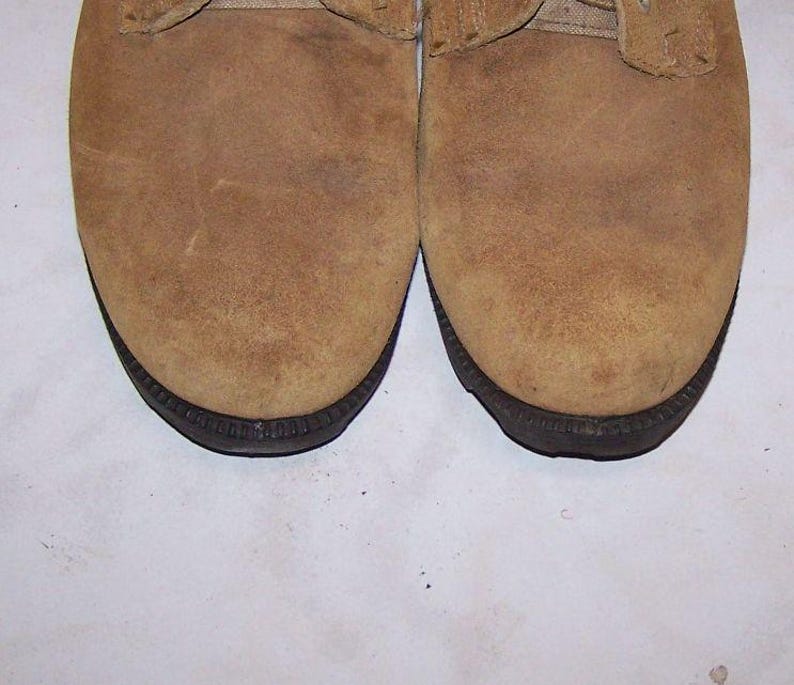 K&ouml;nnte beinhalten: Ein Paar braune Wildlederschuhe mit schwarzen Sohlen. Die Schuhe haben einen Schn&uuml;rverschluss und eine abgerundete Spitze.