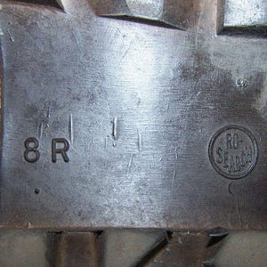 K&ouml;nnte beinhalten: Nahaufnahme einer grauen Metalloberfl&auml;che mit dem Text "8 R" und einem runden Stempel mit der Aufschrift "RO-SEARCH".