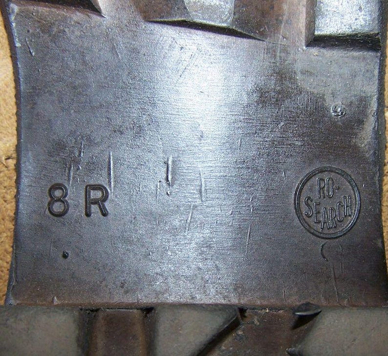 K&ouml;nnte beinhalten: Nahaufnahme einer grauen Metalloberfl&auml;che mit dem Text "8 R" und einem runden Stempel mit der Aufschrift "RO-SEARCH".