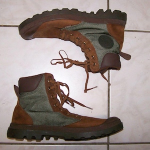May include: Pair of brown and green hiking boots. The boots have a brown suede upper with green canvas panels and brown rubber soles. The boots have brown laces and a padded collar. The soles are thick and have a rugged tread.
