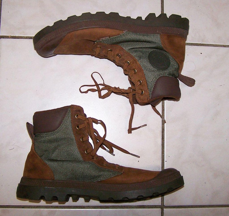 May include: Pair of brown and green hiking boots. The boots have a brown suede upper with green canvas panels and brown rubber soles. The boots have brown laces and a padded collar. The soles are thick and have a rugged tread.