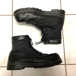 May include: A pair of black tactical boots featuring a combination of smooth leather and fabric panels. These boots have a high-top design with black laces, metal eyelets, and a thick, durable rubber lug sole for traction and support.