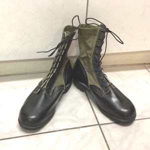 May include: A pair of mid-calf boots featuring black leather lower sections and olive green fabric uppers. The boots have black laces threaded through metal eyelets, a rounded toe, and a thick black rubber sole with a textured tread pattern.