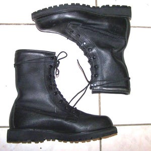 May include: A pair of black leather combat boots featuring a high-top design, thick rubber lug soles, and black laces threaded through metal eyelets. The boots have a smooth finish, a rounded toe, and a structured ankle support for stability.