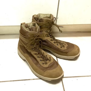 Puede incluir: Un par de botas tácticas de color beige con diseño de caña alta que combina paneles de ante y malla. Las botas incluyen cordones a juego, ojales metálicos, una puntera reforzada y una suela de goma gruesa y resistente para mayor soporte.