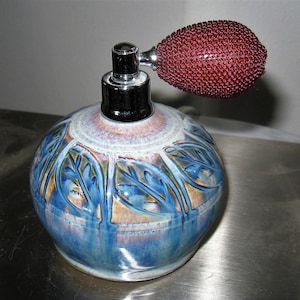 May include: A blue and brown ceramic perfume bottle with a floral design and a red atomizer.