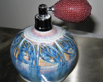 May include: A blue and brown ceramic perfume bottle with a floral design and a red atomizer.