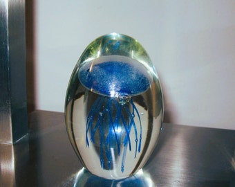 May include: A clear glass paperweight containing a blue jellyfish. The jellyfish has long, flowing tentacles.