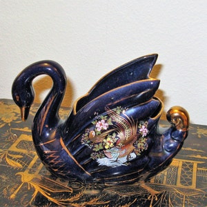 May include: A cobalt blue ceramic swan figurine with gold accents and a painted design of a phoenix and flowers. The swan is shaped like a vase or planter.