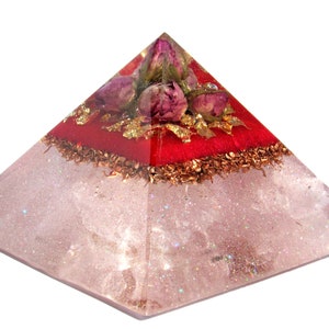 May include: A clear quartz pyramid with a red layer and dried rose buds on top. The pyramid is decorated with gold leaf and copper flakes.
