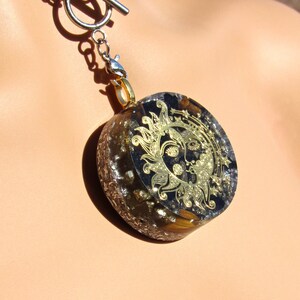 May include: A gold sun and moon pendant necklace with a black and gold background. The pendant is made of resin and has a silver chain.