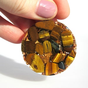 May include: Round, clear resin orb filled with small, irregular pieces of tiger's eye and copper. The orb has a golden brown colour with hints of green and black.