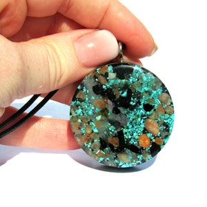 May include: A round pendant necklace with a black cord. The pendant is a mosaic of turquoise, black, and tan stones set in a clear resin. The pendant is approximately 2 inches in diameter.