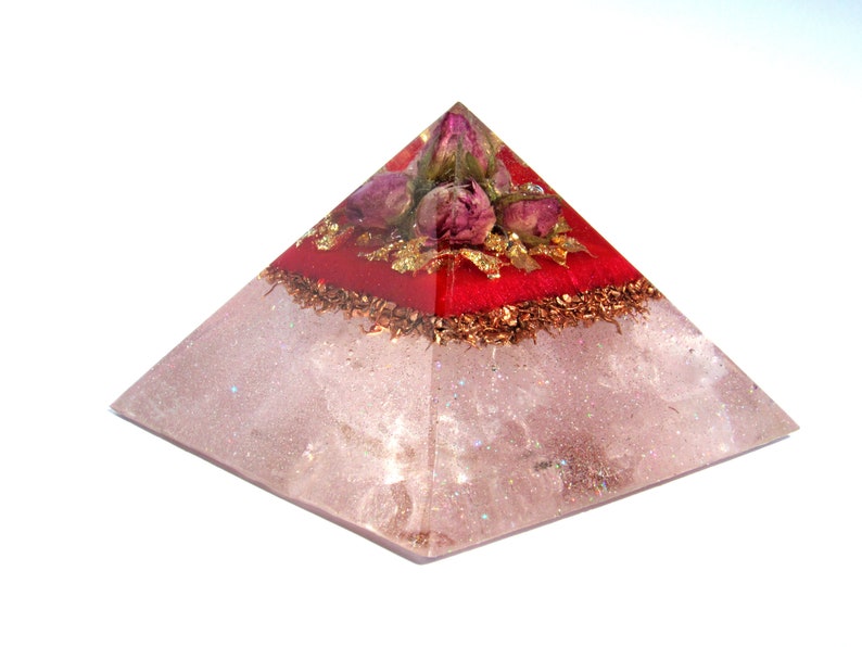 May include: A clear quartz pyramid with a red layer and dried rose buds on top. The pyramid is decorated with gold leaf and copper flakes.