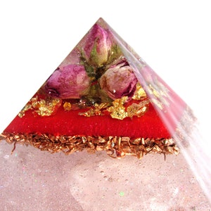 May include: A clear pyramid with a red layer and gold flakes. Dried pink roses are embedded in the top of the pyramid.