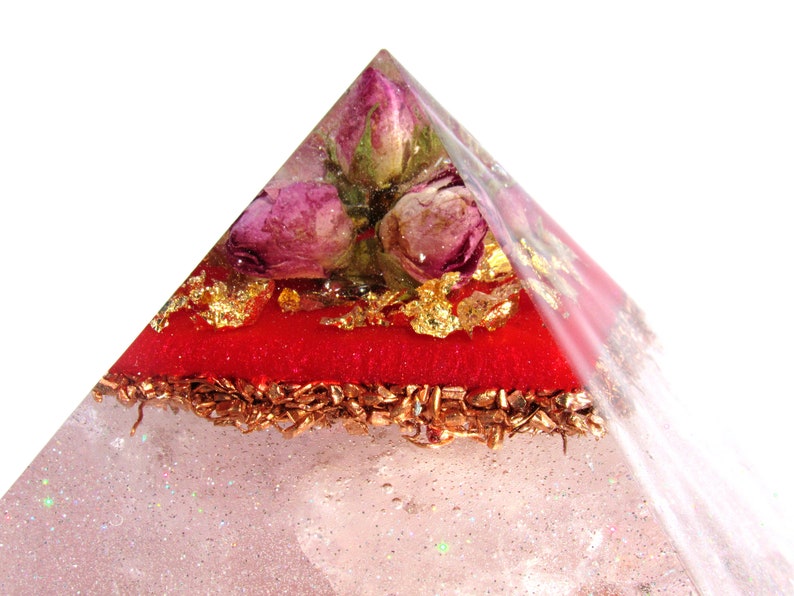 May include: A clear pyramid with a red layer and gold flakes. Dried pink roses are embedded in the top of the pyramid.