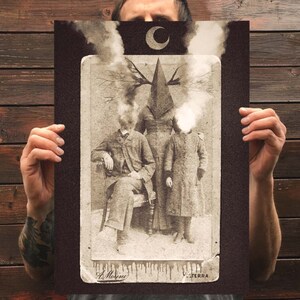 Może przedstawiać: Prostokątny wydruk artystyczny przedstawiający fotografię w stylu vintage w odcieniach sepii, ukazującą trzy postacie. Centralna postać ma głowę w kształcie piramidy z rozgałęzionym porożem. Dwie boczne postacie mają niewyraźne, dymne głowy. Powyżej znajduje się p&oacute;łksiężyc.