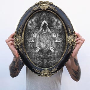 May include: An oval-shaped wall art piece featuring a black and white intricate illustration of a hooded figure surrounded by multiple hands and wings, encased in a decorative black frame with ornate gold-colored filigree accents at the edges.