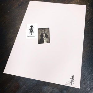 May include: A rectangular white print featuring a small black and white photograph of a person wearing a crown of thorns. The print includes a black logo with the text djangonokes and a matching logo with a signature in the bottom right corner.