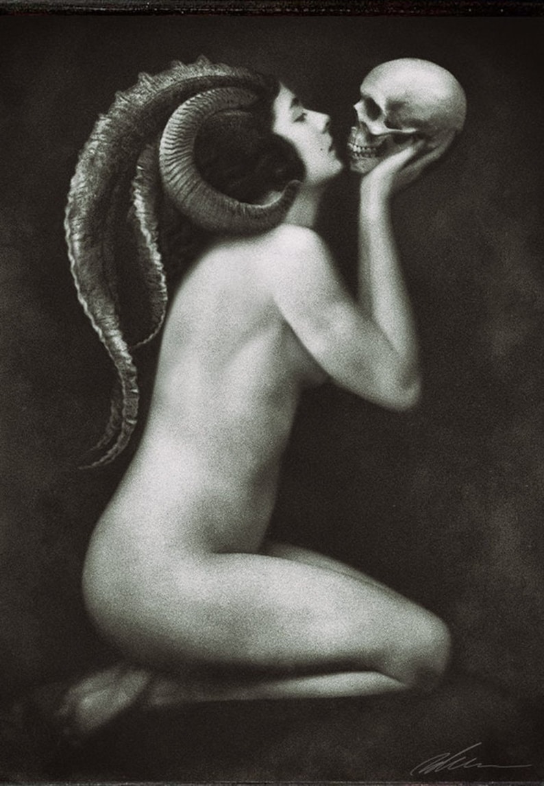 May include: A black and white artistic print depicting a kneeling figure with large, curved ram horns extending from the head. The figure is shown in profile, holding a human skull near the face in a gesture of close proximity against a dark background.