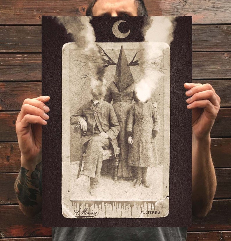 Może przedstawiać: Prostokątny wydruk artystyczny przedstawiający fotografię w stylu vintage w odcieniach sepii, ukazującą trzy postacie. Centralna postać ma głowę w kształcie piramidy z rozgałęzionym porożem. Dwie boczne postacie mają niewyraźne, dymne głowy. Powyżej znajduje się p&oacute;łksiężyc.