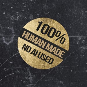 May include: A circular gold foil sticker featuring the black text 100% HUMAN MADE NO AI USED. The sticker has a textured, metallic finish and is set against a dark, distressed charcoal background with visible scratches and surface imperfections.