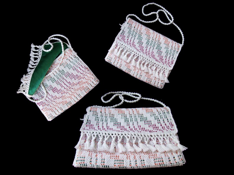 K&ouml;nnte beinhalten: Drei wei&szlig;e geh&auml;kelte Handtaschen mit bunten Mustern und Fransen. Die Handtaschen haben verstellbare Tr&auml;ger und sind aus einer filigranen H&auml;kelarbeit gefertigt.