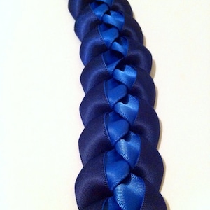 May include: A blue and navy blue braided ribbon lei. The lei is made of two different shades of blue ribbon that are braided together.